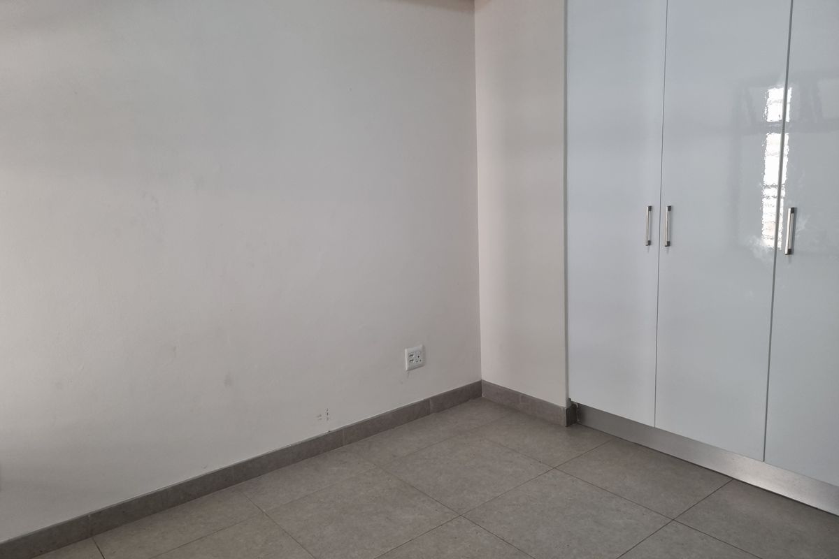 A clean, empty bedroom featuring neutral tiled flooring and modern white built-in cupboards.