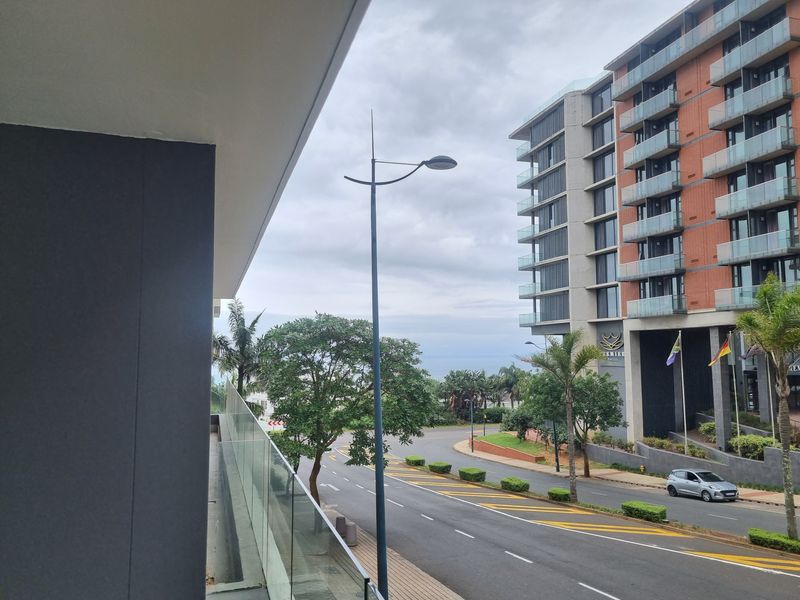 A view from an apartment balcony overlooking a street and neighbouring modern building complex.