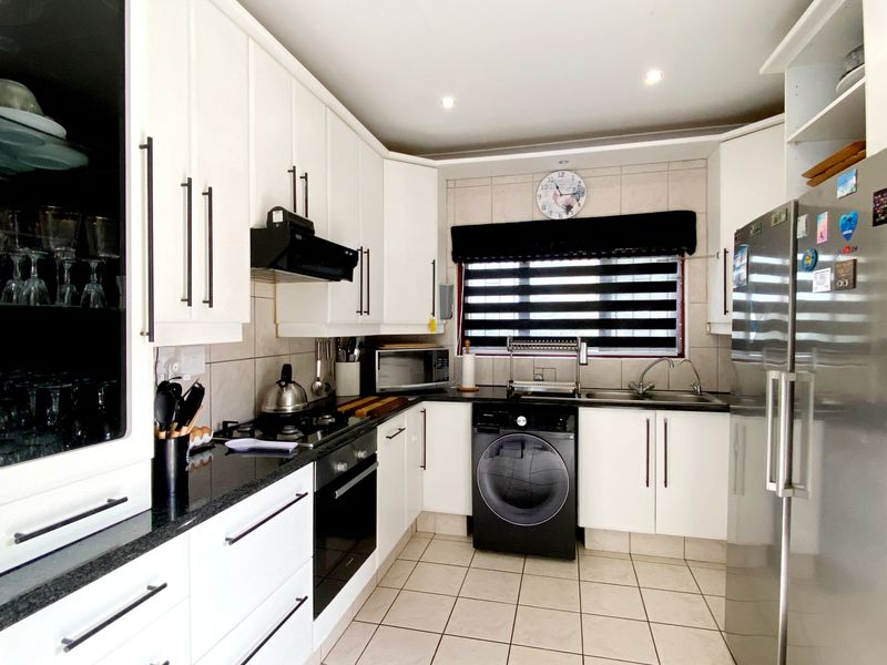 A well-maintained kitchen featuring white cabinetry, granite countertops, a gas hob, built-in oven, and integrated laundry appliance space.