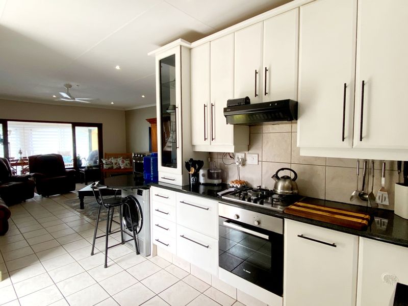 Open-plan kitchen featuring white cabinetry, granite countertops, gas hob, and electric oven, flowing seamlessly into the adjacent living area with tiled flooring throughout.