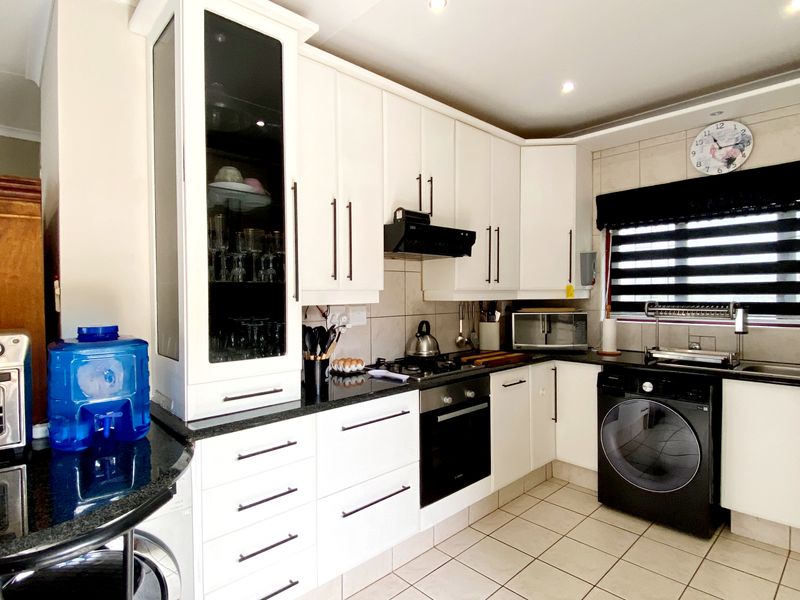 Modern kitchen featuring white cabinetry, granite countertops, gas hob, built-in oven, and tiled flooring with integrated laundry appliance space.