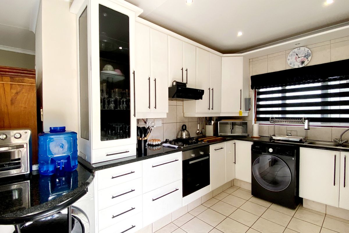 Modern kitchen featuring white cabinetry, granite countertops, gas hob, built-in oven, and tiled flooring with integrated laundry appliance space.