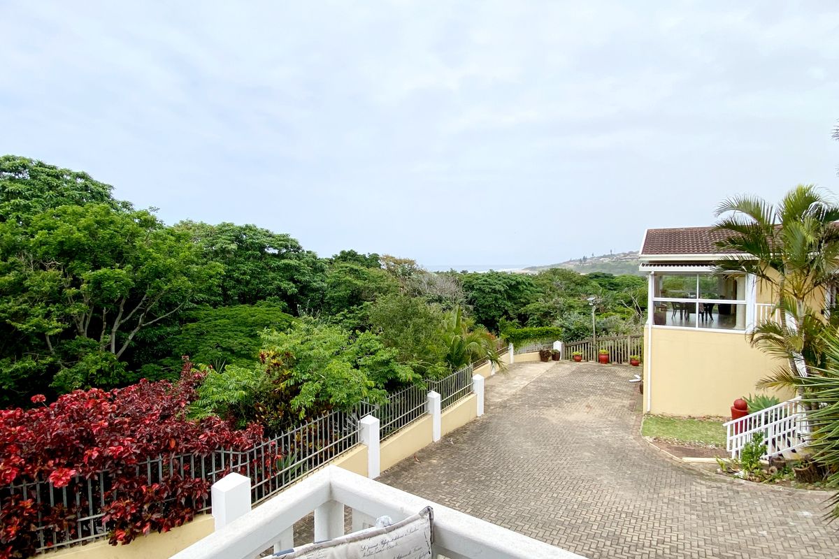 Rear exterior view of the townhouse featuring a paved driveway, perimeter fencing, and lush surrounding greenery with a partial view of the landscape.