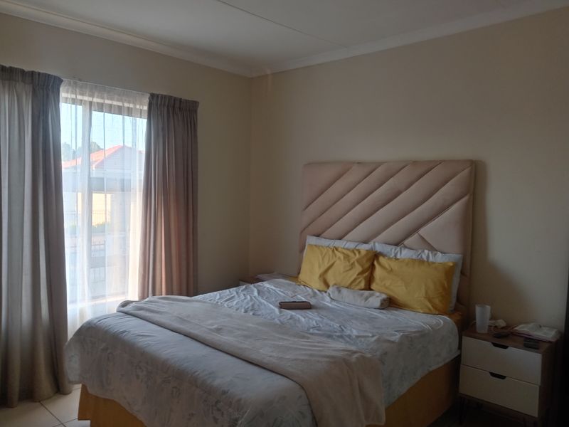 A functional bedroom featuring neutral wall tones, tiled flooring, and large windows with curtain tracks, providing a comfortable and well-lit living space.