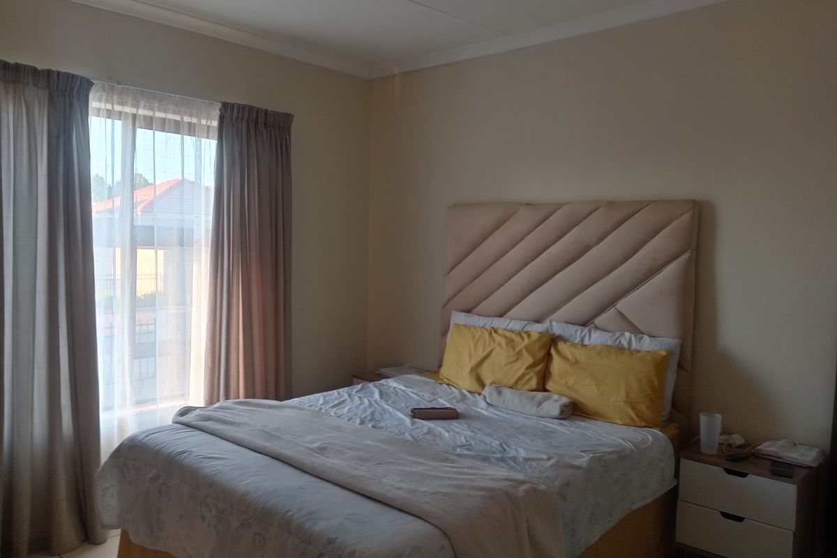 A functional bedroom featuring neutral wall tones, tiled flooring, and large windows with curtain tracks, providing a comfortable and well-lit living space.