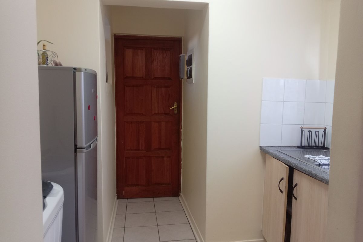 A functional kitchen area featuring tiled flooring, laminate cabinetry, a stone-look countertop with a tiled splashback, and a solid timber door.