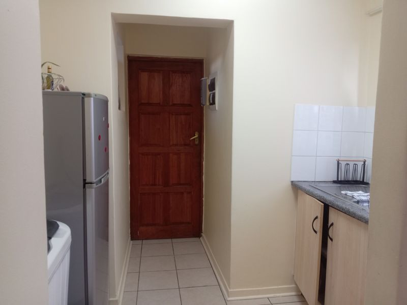 A functional kitchen area featuring tiled flooring, laminate cabinetry, a stone-look countertop with a tiled splashback, and a solid timber door.