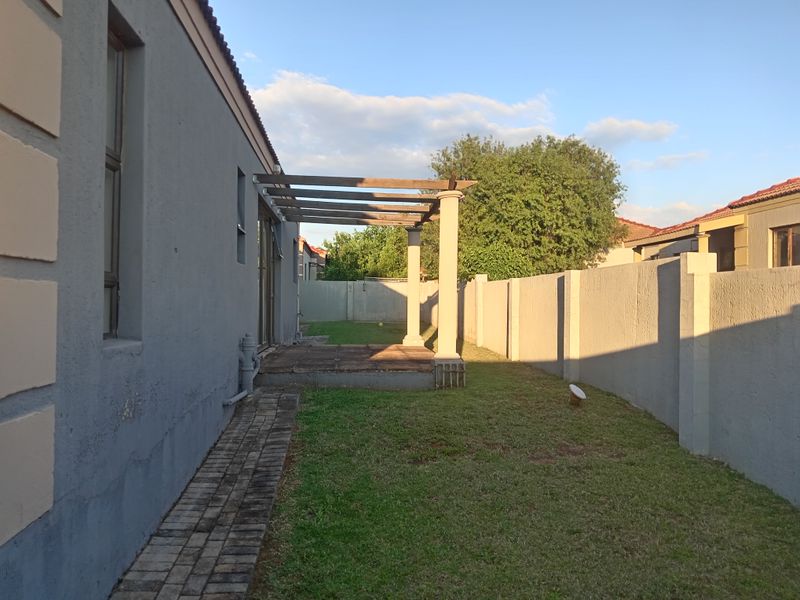 Rear exterior view of the townhouse featuring a small lawn, a paved walkway, and a pergola structure attached to the building.