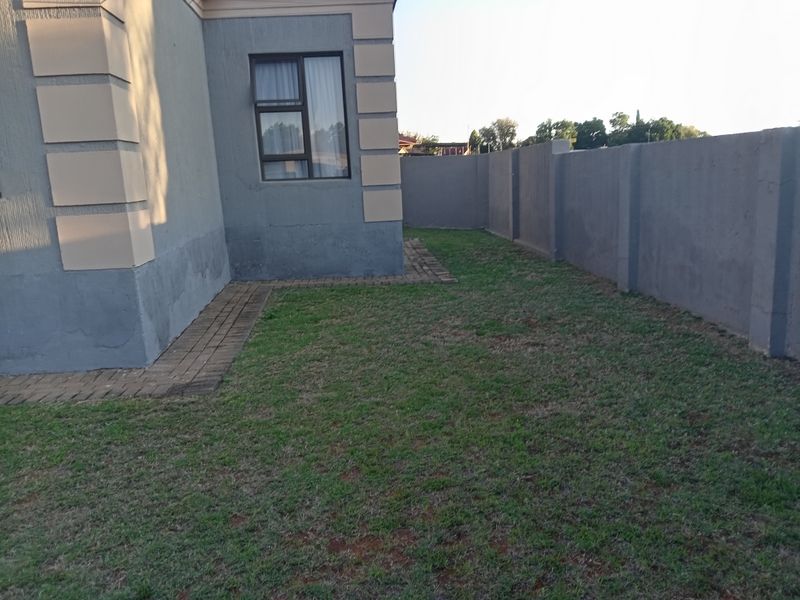 A view of the rear garden area featuring a lawn, paved walkway, and perimeter wall, with visible exterior wall finishes.
