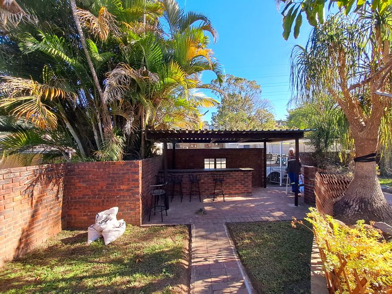 Outdoor entertainment area featuring a built-in brick bar, timber pergola roof, and paved patio space set within a landscaped garden.