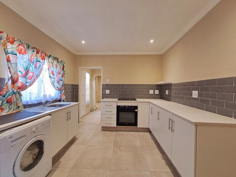 A functional kitchen featuring white cabinetry, a built-in oven with gas hob, grey tiled backsplash, and neutral floor tiles.