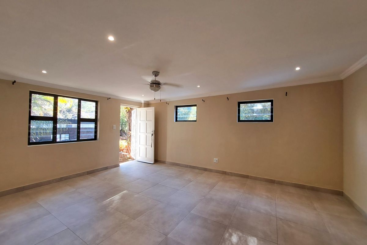 A bright and spacious living area featuring neutral tiled flooring, recessed downlighting, a ceiling fan, and direct access to the exterior.