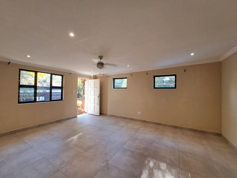 A bright and spacious living area featuring neutral tiled flooring, recessed downlighting, a ceiling fan, and direct access to the exterior.