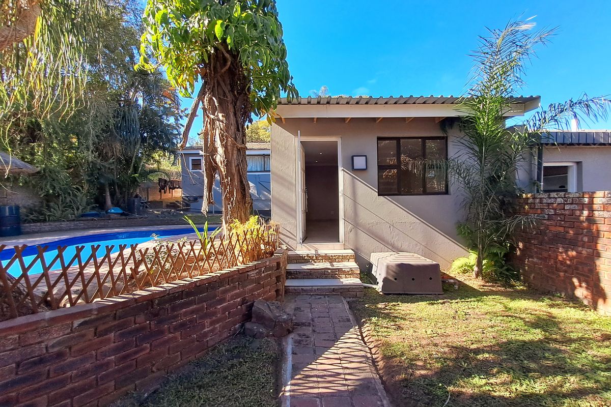 Rear view of the cottage featuring a swimming pool, brick boundary wall, and a paved walkway leading to the entrance.