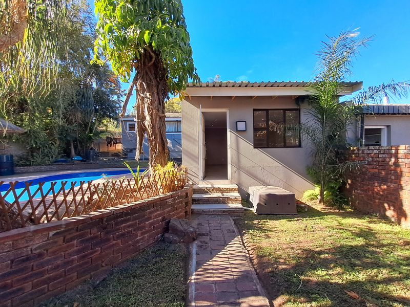 Rear view of the cottage featuring a swimming pool, brick boundary wall, and a paved walkway leading to the entrance.