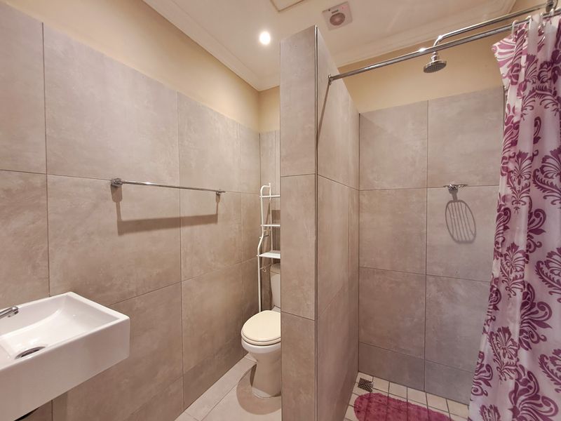 A modern bathroom featuring large-format neutral wall tiles, a wall-mounted basin, a toilet, and a shower area with a fixed shower head.
