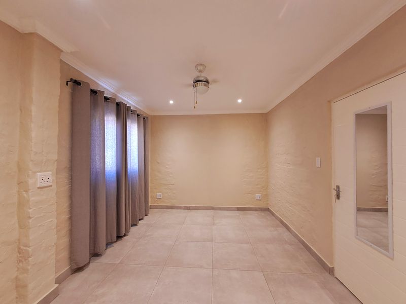 A clean, empty bedroom featuring neutral textured walls, large format floor tiles, recessed lighting, and a ceiling fan.