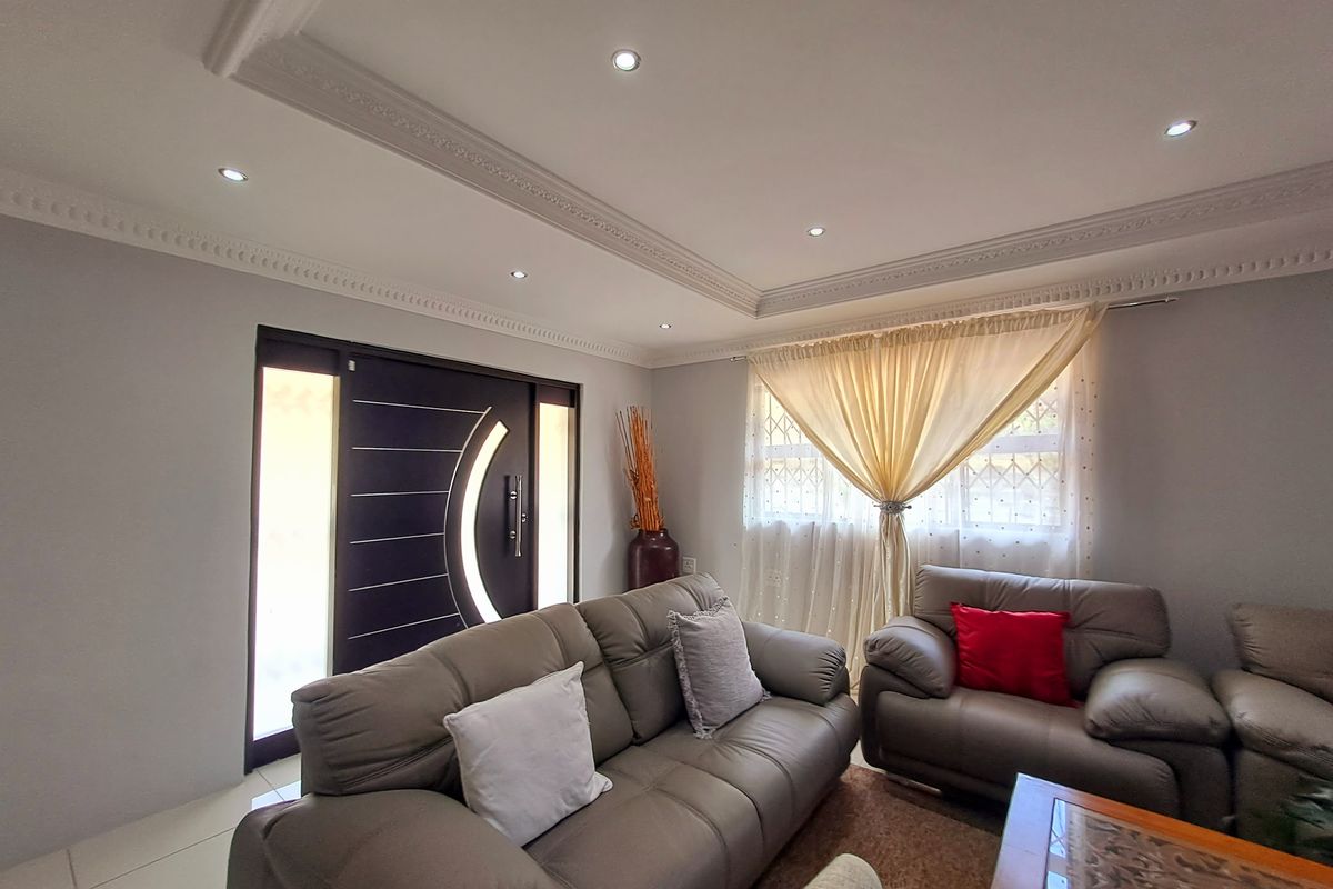 A well-maintained living room featuring decorative ceiling cornices, recessed downlighting, and a modern entrance door with side panels.