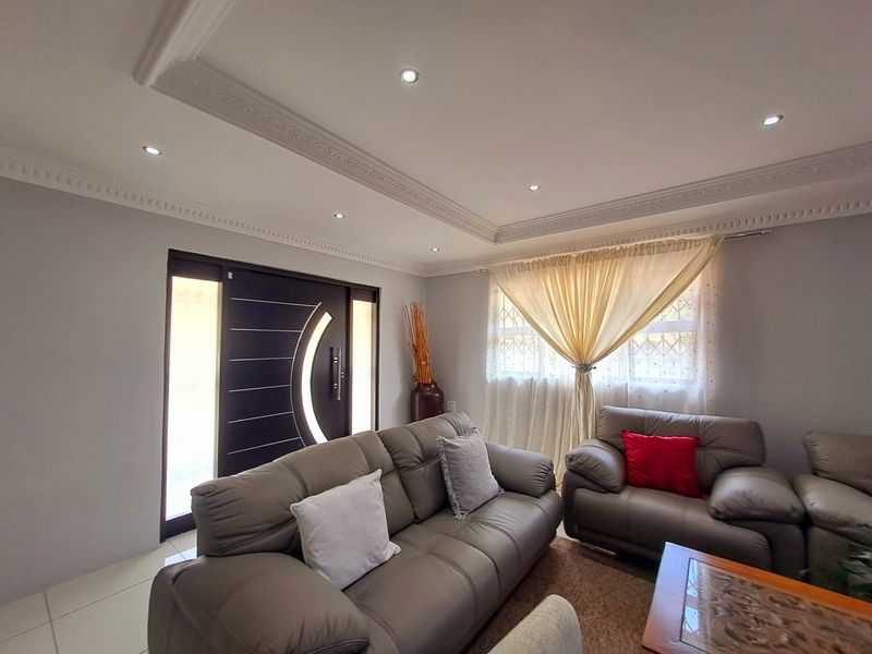 A well-maintained living room featuring decorative ceiling cornices, recessed downlighting, and a modern entrance door with side panels.