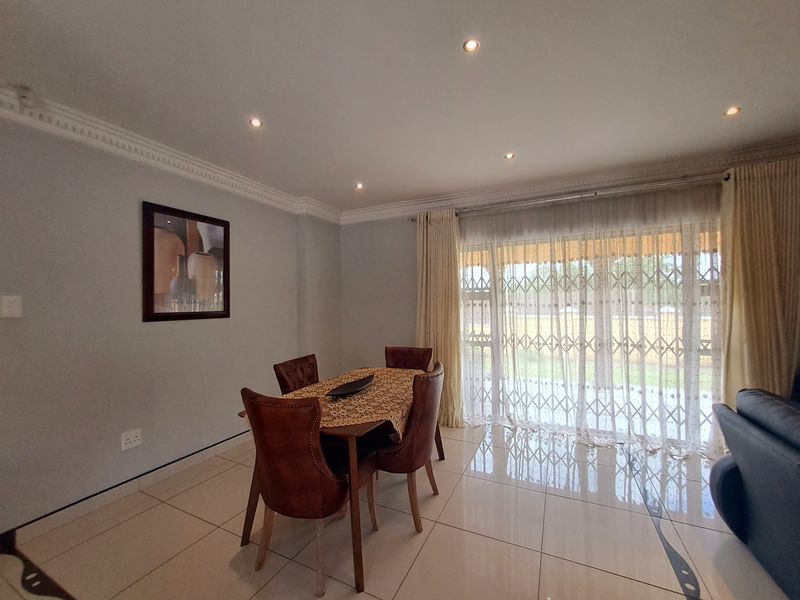 A bright dining area featuring polished porcelain floor tiles, elegant crown molding, recessed downlights, and a sliding glass door with an integrated security gate.