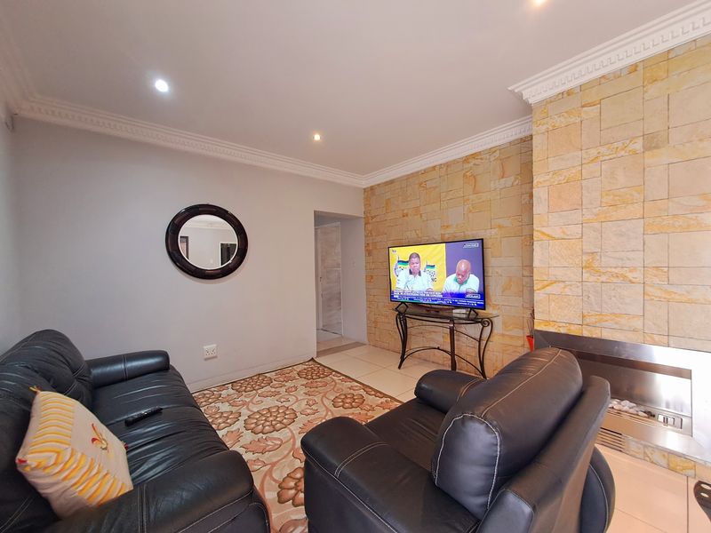 A comfortable living room featuring a striking stone-clad feature wall with a built-in fireplace, complemented by decorative ceiling cornices and recessed lighting.
