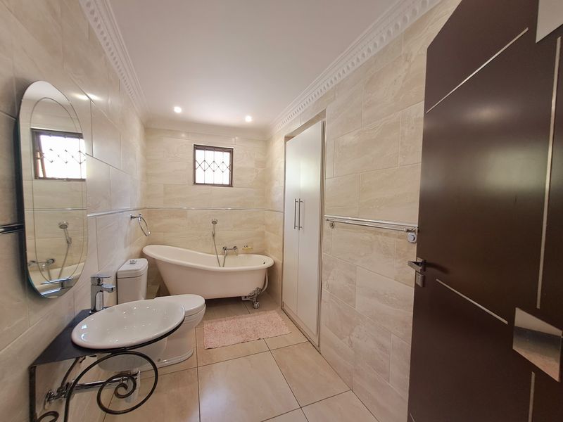 A well-maintained bathroom featuring a freestanding bathtub, ceramic basin, toilet, and neutral floor-to-ceiling wall tiles with built-in storage.