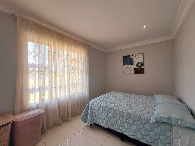 A well-maintained bedroom featuring neutral tiled flooring, recessed downlighting, and decorative cornice detailing.