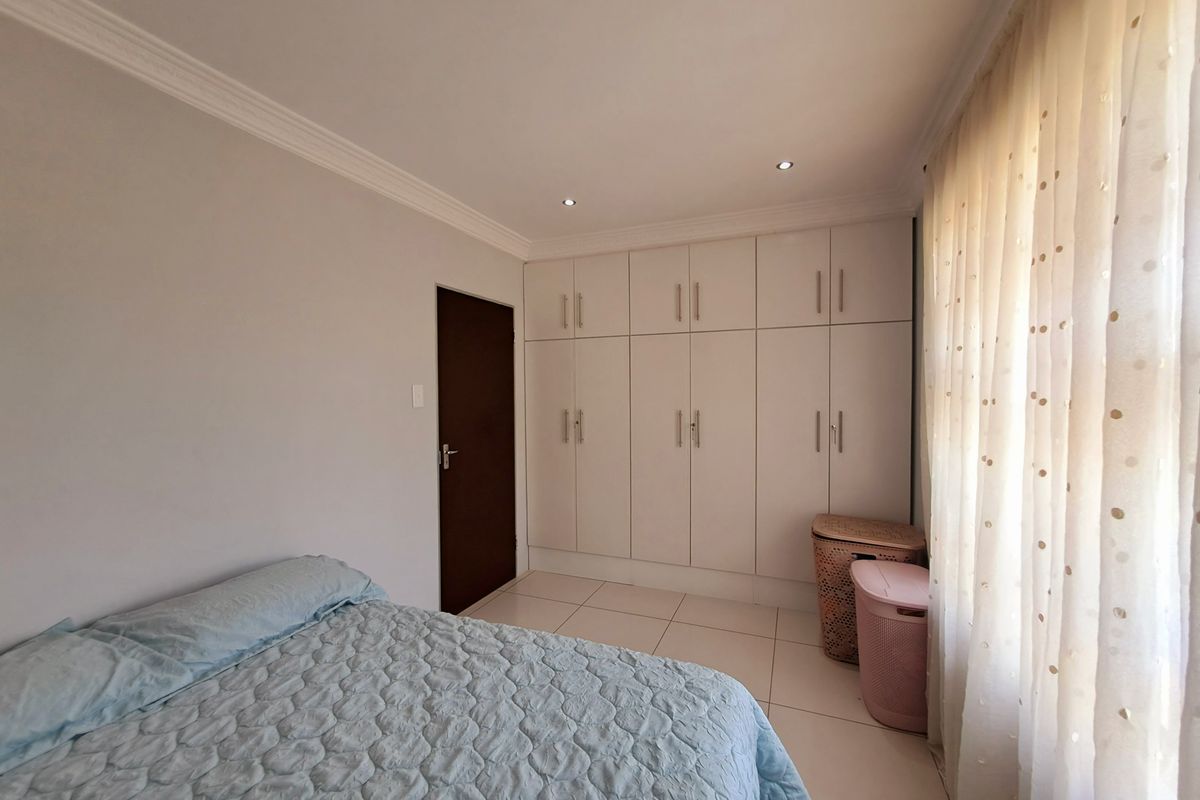 A well-maintained bedroom featuring neutral tiled flooring, ample built-in cupboard storage, recessed downlighting, and decorative ceiling cornicing.