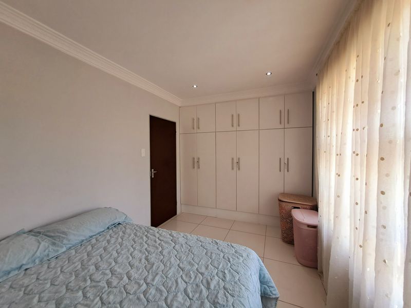 A well-maintained bedroom featuring neutral tiled flooring, ample built-in cupboard storage, recessed downlighting, and decorative ceiling cornicing.