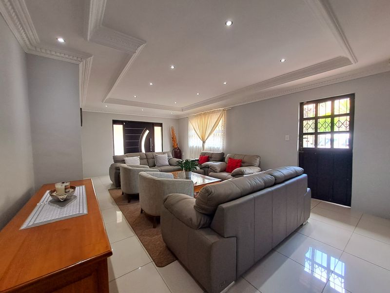Spacious living room featuring modern tiled flooring, decorative ceiling cornicing with recessed lighting, and a secure entrance door.