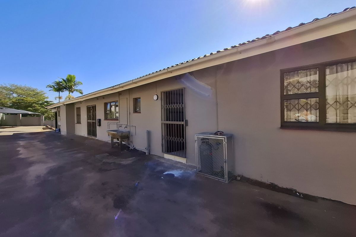 Rear exterior view of the house featuring a concrete driveway, security gates, and a utility wash basin area.