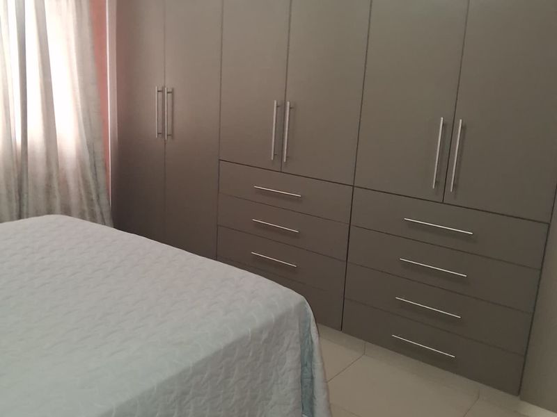 A bedroom featuring extensive floor-to-ceiling built-in cupboards with modern hardware and neutral tiled flooring.