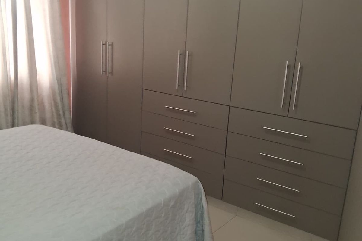 A bedroom featuring extensive floor-to-ceiling built-in cupboards with modern hardware and neutral tiled flooring.