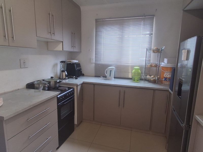 A functional kitchen featuring neutral-toned built-in cabinetry, laminate countertops, tiled flooring, and a freestanding stove, offering a clean and practical workspace.