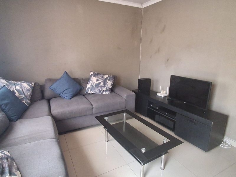 A living room featuring tiled flooring and coved ceilings, currently showing signs of wall surface wear and staining.