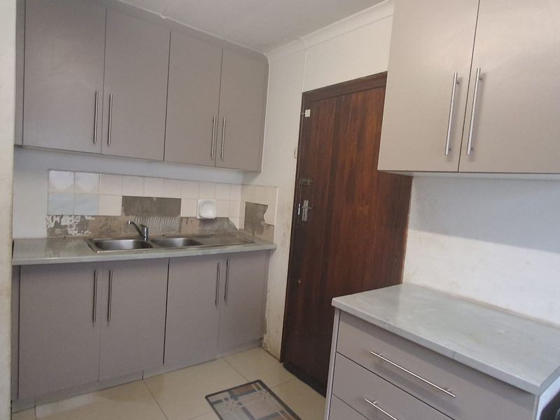 A compact kitchen featuring grey built-in cabinetry, laminate countertops, and a double sink, requiring minor finishing work to the backsplash and wall surfaces.