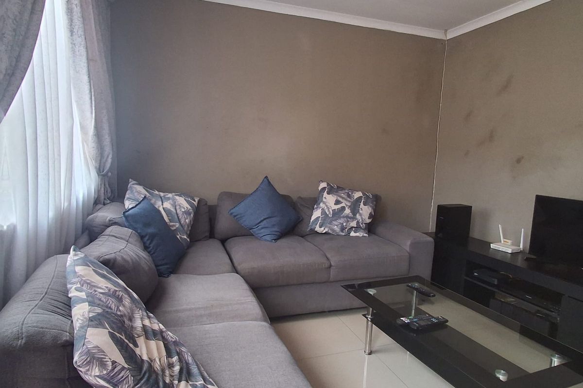 A living room featuring tiled flooring and neutral wall tones, currently showing signs of wear on the wall surfaces.
