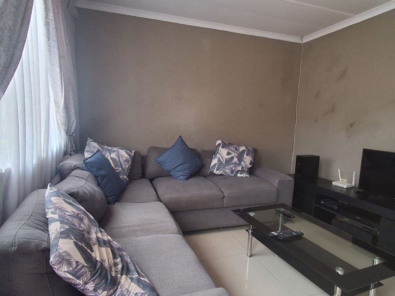 A living room featuring tiled flooring and neutral wall tones, currently showing signs of wear on the wall surfaces.