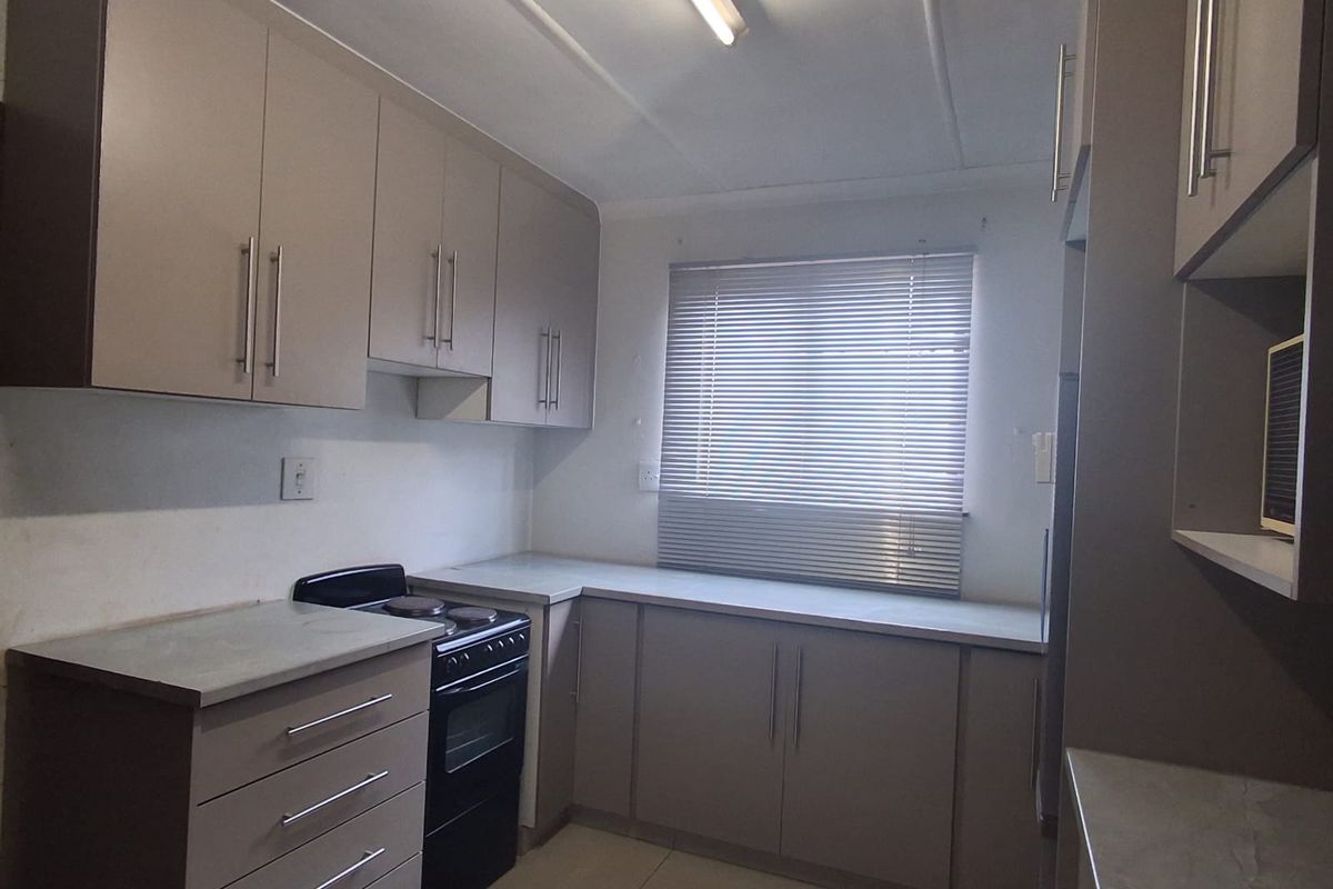 A functional kitchen featuring neutral-toned built-in cabinetry, laminate countertops, tiled flooring, and a freestanding stove, offering a clean and practical workspace.