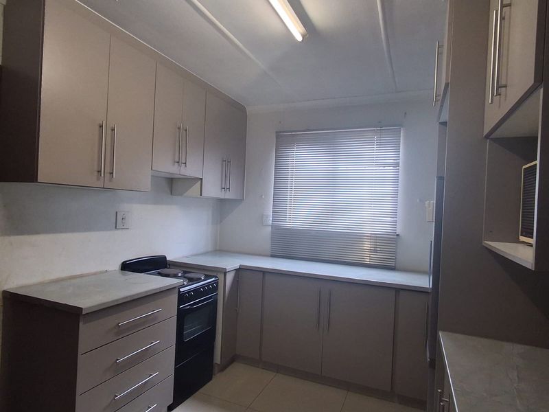 A functional kitchen featuring neutral-toned built-in cabinetry, laminate countertops, tiled flooring, and a freestanding stove, offering a clean and practical workspace.