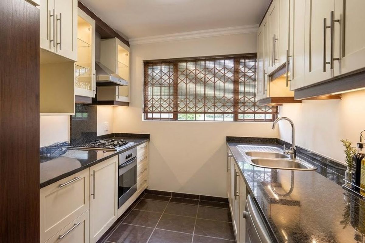 Modern galley-style kitchen featuring granite countertops, shaker-style cabinetry, built-in oven with gas hob, and integrated under-cabinet lighting.