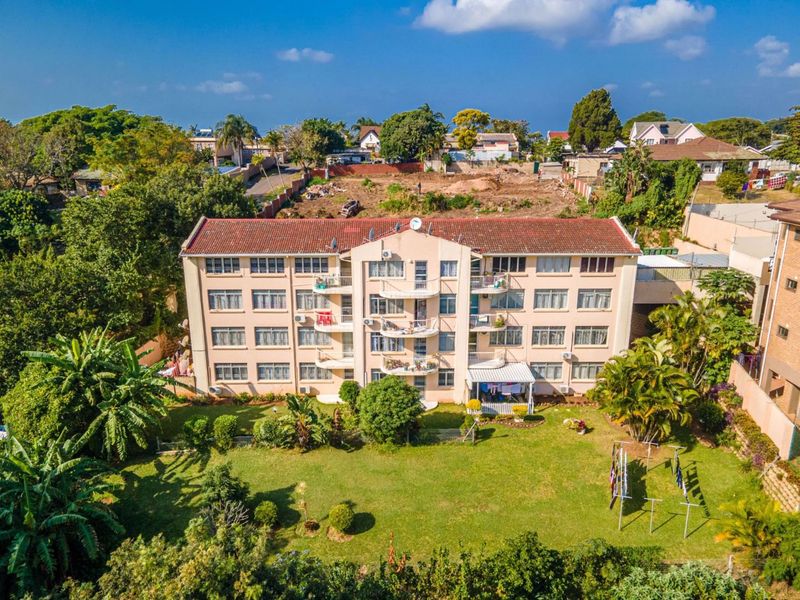 Aerial view of a multi-story residential flat complex featuring a large communal garden, private balconies, and established surrounding greenery.