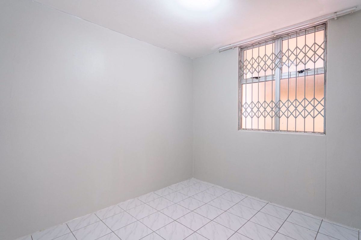 An empty bedroom featuring tiled flooring and a window fitted with a security gate.