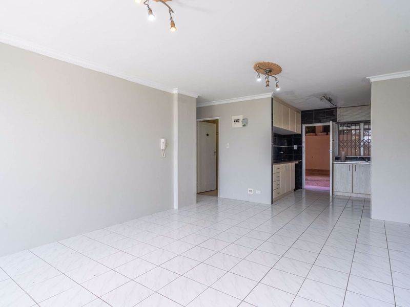 Open-plan living area featuring tiled flooring and an integrated kitchen space with built-in cabinetry, offering a blank canvas for interior design.