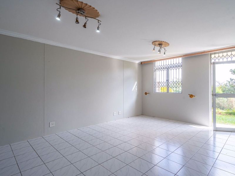 A bright, empty living room featuring white tiled flooring, decorative ceiling lights, and a secure door leading to the exterior.