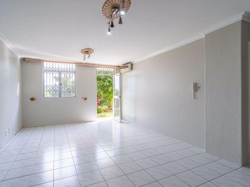 A bright, empty living area featuring tiled flooring, decorative ceiling roses, cornicing, an intercom system, and direct access to an outdoor space.