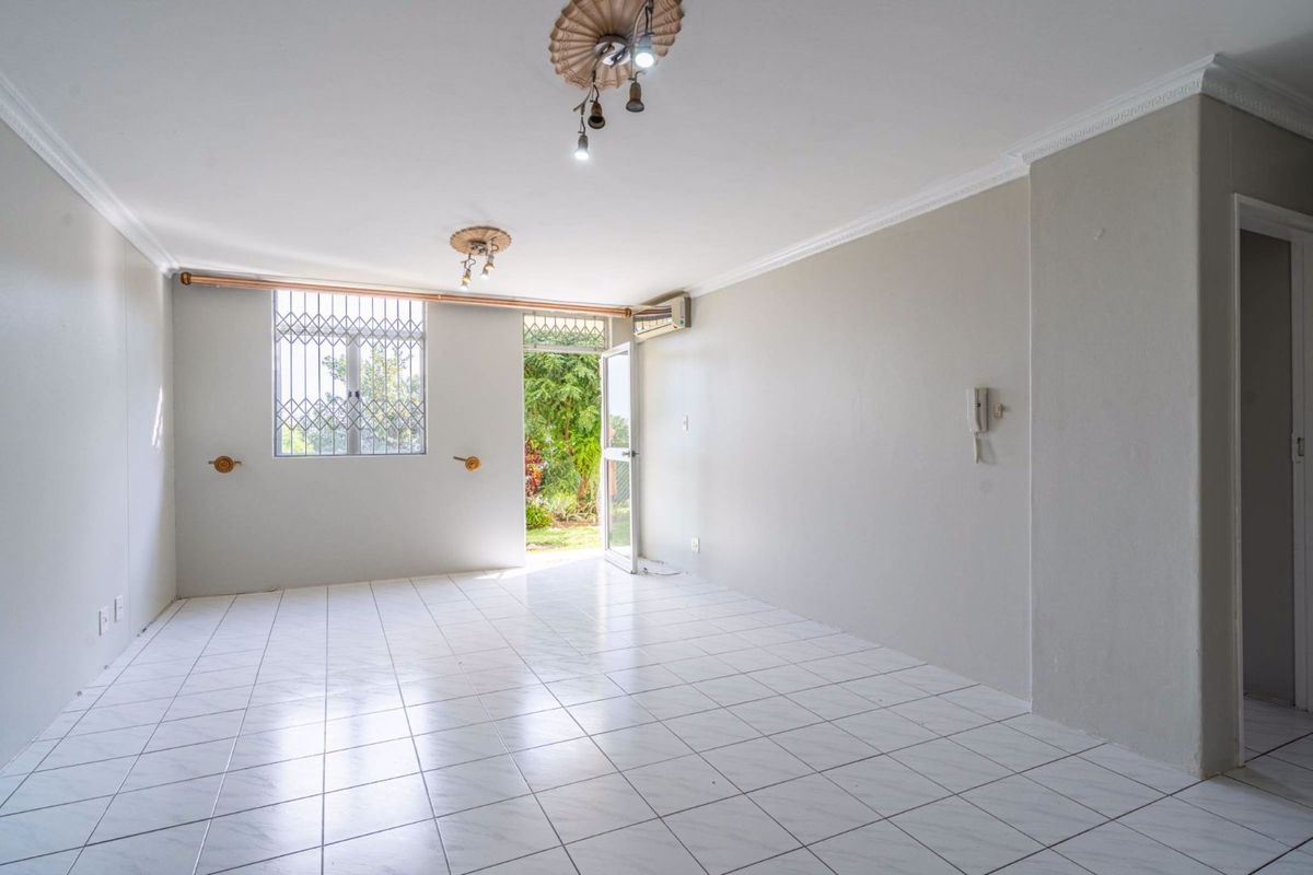 A bright, empty living area featuring tiled flooring, decorative ceiling roses, cornicing, an intercom system, and direct access to an outdoor space.