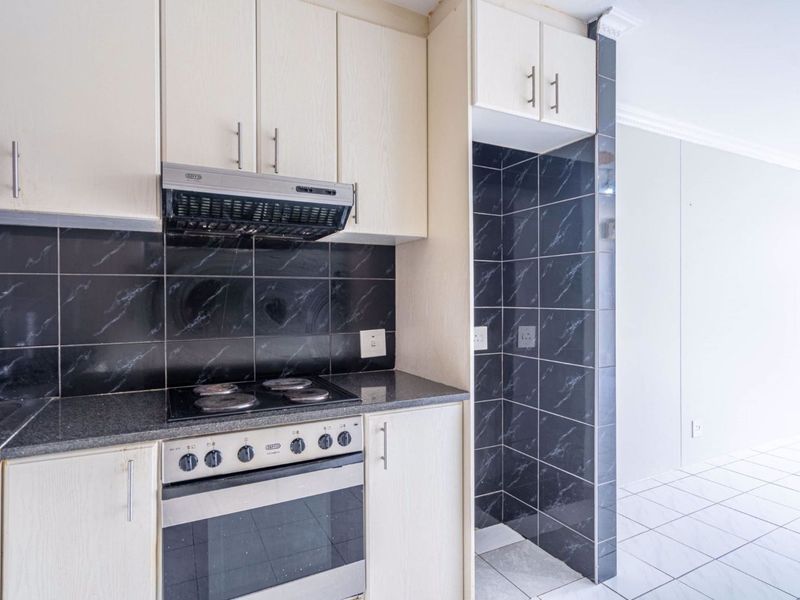 A clean, functional kitchen featuring light-toned cabinetry, granite countertops, a built-in oven with hob, and a modern black tiled backsplash.