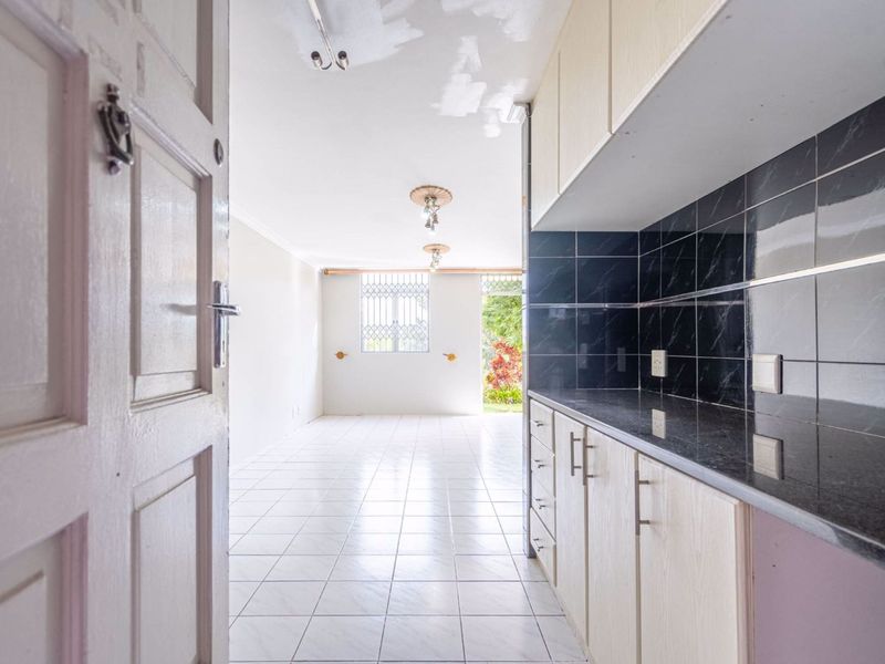 An open-plan living and kitchen area featuring tiled floors, granite countertops, and dark tiled backsplash, requiring minor ceiling repairs.