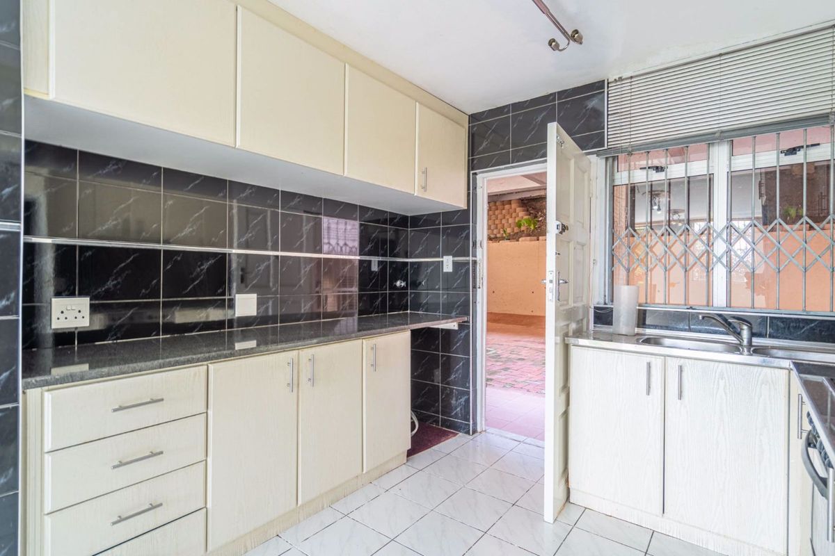 A functional kitchen featuring built-in cabinetry, granite countertops, a stainless steel sink, and dark tiled backsplash with direct access to an outdoor area.